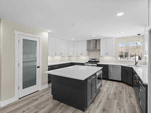 Kitchen featuring sink, white cabinetry, appliances with stainless steel finishes, a kitchen island, and wall chimney range hood