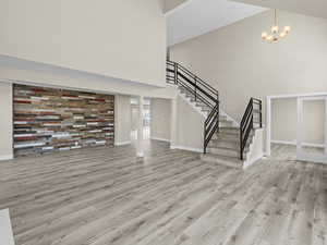 Unfurnished living room with a towering ceiling, light hardwood / wood-style flooring, and a notable chandelier