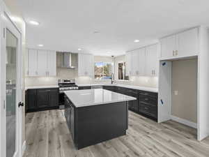 Kitchen featuring sink, white cabinetry, a center island, appliances with stainless steel finishes, and wall chimney range hood