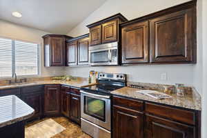 Kitchen with stainless steel appliances, , lofted ceiling, sink, light stone counters, and dark brown cabinets