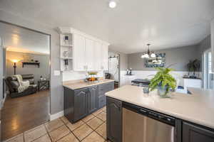 Kitchen with dishwasher, white cabinets, light tile patterned floors, and a textured ceiling