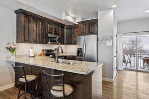 Kitchen featuring dark brown cabinetry, stainless steel appliances, dark hardwood / wood-style flooring, and kitchen peninsula