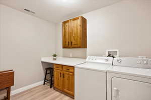 Washroom featuring cabinets, washing machine and dryer, and light hardwood / wood-style floors