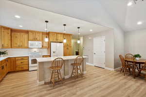 Kitchen with a kitchen island, decorative light fixtures, tasteful backsplash, white appliances, and light wood-type flooring