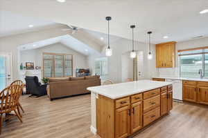 Kitchen featuring sink, light wood-type flooring, white dishwasher, a kitchen island, and pendant lighting