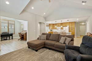 Living room with ceiling fan, high vaulted ceiling, and light wood-type flooring