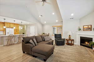 Living room featuring high vaulted ceiling, a tile fireplace, ceiling fan, and light wood-type flooring