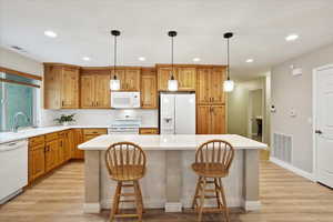 Kitchen featuring sink, a breakfast bar area, a kitchen island, pendant lighting, and white appliances