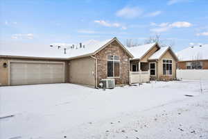 Snow covered rear of property with a garage and central AC