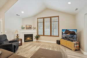 Living room featuring a premium fireplace, lofted ceiling, and light hardwood / wood-style flooring