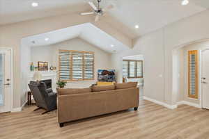 Living room with ceiling fan, lofted ceiling, and light wood-type flooring