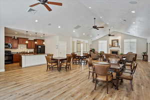 Dining room with vaulted ceiling, light hardwood / wood-style flooring, a textured ceiling, ceiling fan, and a tiled fireplace