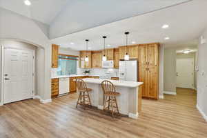 Kitchen featuring a breakfast bar, a center island, pendant lighting, white appliances, and light hardwood / wood-style floors