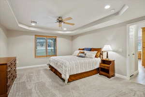 Carpeted bedroom with a raised ceiling and ceiling fan