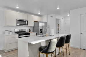 Kitchen featuring sink, white cabinets, a kitchen island with sink, stainless steel appliances, and light wood-type flooring