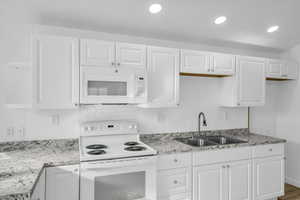 Kitchen with light stone countertops, sink, white cabinets, and white appliances