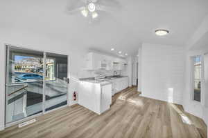 Kitchen featuring sink, white appliances, light hardwood / wood-style flooring, white cabinetry, and vaulted ceiling