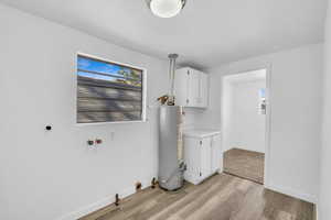 Washroom with cabinets, light wood-type flooring, and gas water heater