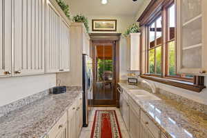 Kitchen with stainless steel appliances, light stone countertops, cream cabinets, and sink