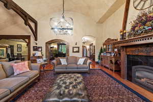 Living room featuring lofted ceiling, a notable chandelier, a tiled fireplace, and wood-type flooring