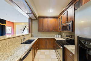 Kitchen with light stone counters, sink, and appliances with stainless steel finishes