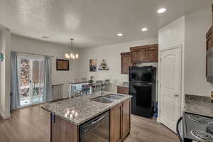 Kitchen with decorative light fixtures, sink, an island with sink, and black appliances