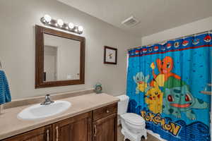 Bathroom with a textured ceiling, toilet, a shower with curtain, and vanity