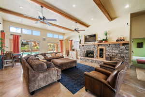 Living room with ceiling fan, beam ceiling, a towering ceiling, and a fireplace