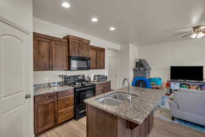 Kitchen with light stone countertops, black appliances, sink, light wood-type flooring, and a center island with sink