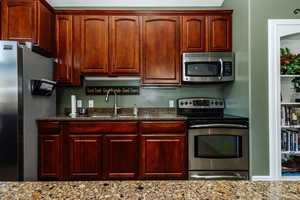 Clubhouse Kitchen with light stone counters, stainless steel appliances, and sink