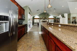 Clubhouse Kitchen featuring appliances with stainless steel finishes, tile patterned flooring, hanging light fixtures, light stone counters, and vaulted ceiling