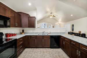 Kitchen with sink, black appliances, light stone countertops, vaulted ceiling, and kitchen peninsula