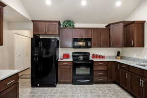 Kitchen featuring light stone counters, lofted ceiling, dark brown cabinets, and black appliances