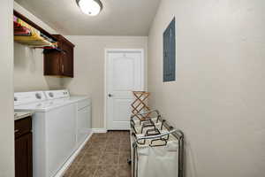 Clothes washing area with washer and clothes dryer, electric panel, cabinets, a textured ceiling, and dark tile patterned flooring