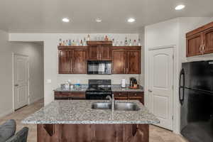 Kitchen featuring light stone counters, sink, black appliances, and an island with sink