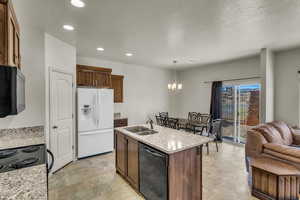 Kitchen featuring black appliances, an inviting chandelier, sink, hanging light fixtures, and light stone counters