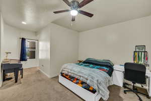 Bedroom with ceiling fan, light colored carpet, and a textured ceiling