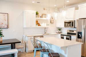 Kitchen with pendant lighting, sink, white cabinetry, stainless steel appliances, and a center island