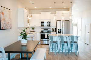 Kitchen featuring sink, appliances with stainless steel finishes, white cabinets, a kitchen island, and decorative light fixtures