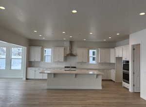 Kitchen with white cabinetry, wall chimney range hood, and a center island with sink