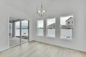 Unfurnished dining area featuring lofted ceiling, a notable chandelier, and light hardwood / wood-style floors