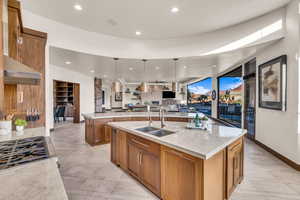 Kitchen featuring extractor fan, pendant lighting, sink, a kitchen island with sink, and light stone countertops