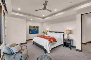 Carpeted bedroom featuring a raised ceiling and ceiling fan