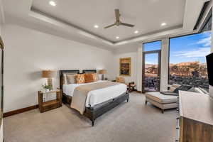 Bedroom with ceiling fan, light colored carpet, a raised ceiling, and access to outside