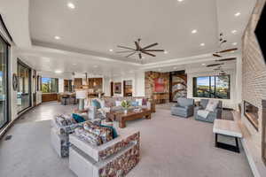 Living room with ceiling fan, a tray ceiling, a fireplace, and light carpet