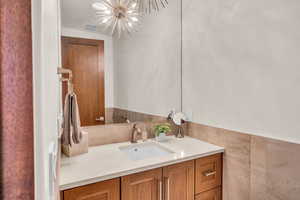 Bathroom with an inviting chandelier, vanity, and tile walls