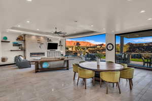 Dining room featuring ceiling fan, a large fireplace, a tray ceiling, and a wall of windows