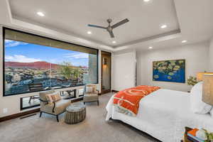 Bedroom with a raised ceiling, ceiling fan, and carpet flooring