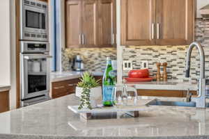 Kitchen with light stone counters, sink, tasteful backsplash, and appliances with stainless steel finishes