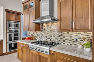 Kitchen with light tile patterned floors, stainless steel appliances, light stone countertops, decorative backsplash, and wall chimney range hood